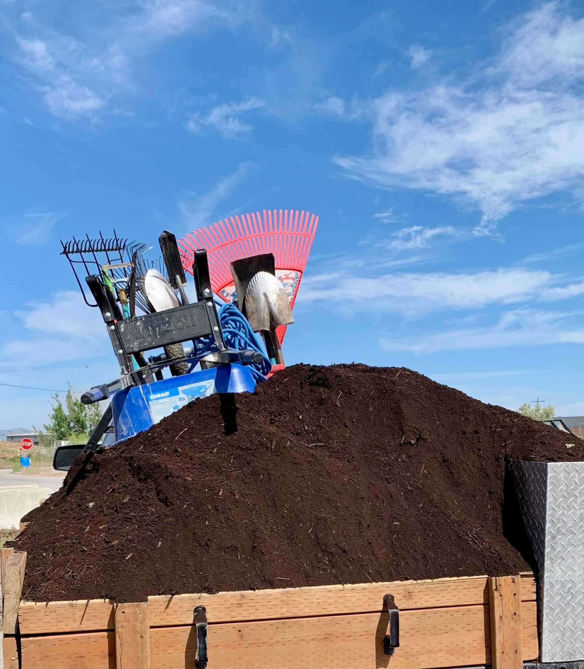 A truck bed loaded with compost and mulch, with rakes and shovels ready to unload